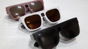 Imagen de las gafas Relúmino en la que aparecen tres modelos de distintos colores: uno rojo, otro blanco y otro negro. Visualmente se asemejan mucho a unas gafas de sol clásicas con patillas anchas, con la salvedad de que en el puente se aprecia el orificio de la Cámara de video.