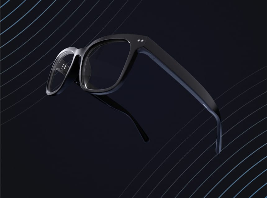 La imagen muestra unas gafas inteligentes sobre un fondo con líneas diagonales que crean una sensación de profundidad y dinamismo. Las gafas tienen un diseño moderno y elegante con montura negra. En la patilla derecha de las gafas, se pueden observar varios botones o sensores, lo que sugiere funcionalidades interactivas o controles táctiles. El diseño general es minimalista y funcional, enfocándose en la integración discreta de la tecnología en un accesorio cotidiano.