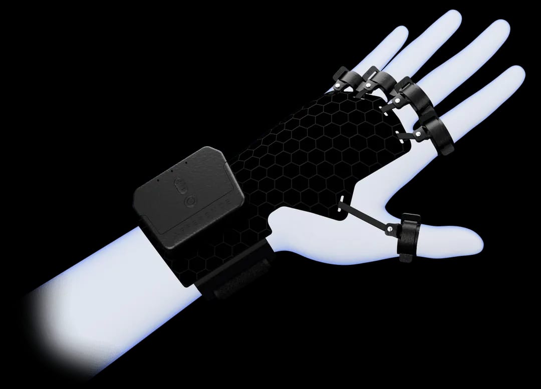 La imagen muestra un dispositivo wearable en forma de guante que cubre toda la palma, la muñeca y se extiende parcialmente por el antebrazo. El guante tiene una estructura de color negro con un patrón de panal sobre la palma y sujeciones que parecen estar aseguradas sobre los dedos y la muñeca. Hay un módulo rectangular, también en negro, que se encuentra sobre el dorso de la mano, presumiblemente conteniendo la electrónica principal del dispositivo. El diseño del dispositivo sugiere funcionalidad avanzada, como retroalimentaciónháptica, seguimiento de movimiento, o alguna forma de control de interfaz para interacciones de realidad virtual o aumentada. El aspecto general es moderno y sofisticado, indicando un producto de alta tecnología diseñado para la interactividad inmersiva o para mejorar la interacción con el entorno digital.
