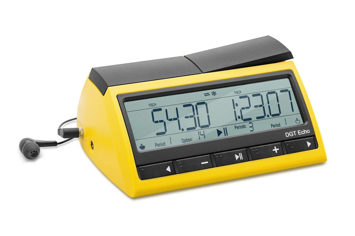 La imagen muestra un reloj parlante DGT ECHO rectangular con bordes reddondeados de color amarillo con una pantalla digital grande que marca las 12:07. La pantalla tiene números digitales de estilo moderno, y hay iconos adicionales que representan alarmas u otras funciones. A los lados de la pantalla, hay dos altavoces pequeños, indicativos de su función de habla. Debajo del reloj, se ven unos auriculares negros con almohadillas redondas, presumiblemente para uso privado del audio del reloj. El fondo de la imagen es blanco, lo que resalta el color amarillo del dispositivo.