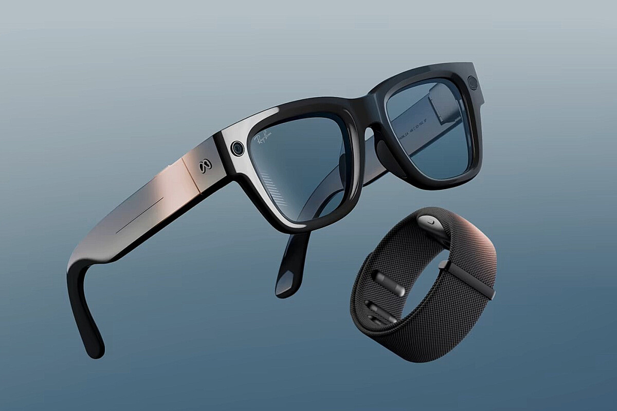 En la imagen se muestra un conjunto formado por unas gafas inteligentes y una pulsera de control, ambos con un diseño moderno, técnico y sofisticado. Las gafas Meta Ray-Ban Display • Montura: De estilo Ray-Ban clásico, con forma cuadrada y robusta. La parte frontal es negra brillante y bastante sólida, transmitiendo resistencia y un aire tecnológico que rompe ligeramente con la elegancia discreta de unas gafas de calle tradicionales. • Patillas: Más gruesas de lo habitual en unas gafas convencionales, con un acabado en degradado metálico que pasa de un tono negro a un gris acerado con reflejos cobrizos. En la unión de la patilla con la montura aparece grabado el logotipo de Meta (∞), muy visible, reforzando la identidad tecnológica. • Componentes integrados: Se distingue claramente una cámara frontal en la esquina de la montura, junto a la lente derecha, diseñada para capturar fotos y vídeo. También se aprecian posibles micrófonos y sensores en las patillas, así como las bisagras reforzadas para sostener la electrónica. • Lentes: De color azul oscuro con efecto ahumado, aportan un estilo moderno y urbano. Reflejan la integración de una pantalla interna que pasa desapercibida desde el exterior. La pulsera Meta Neural Band • Diseño: De aspecto minimalista y técnico. Está fabricada con una malla texturizada de material sintético (probablemente Vectran), en color negro mate con ligeros brillos metálicos. • Cierre: Sistema de ajuste similar al de algunas pulseras deportivas, con un pasador integrado que se inserta en las ranuras para adaptarse a la muñeca. • Módulo central: Sobresale ligeramente en la parte superior de la pulsera, con un pequeño LED o botón de estado visible, que delata su naturaleza electrónica.