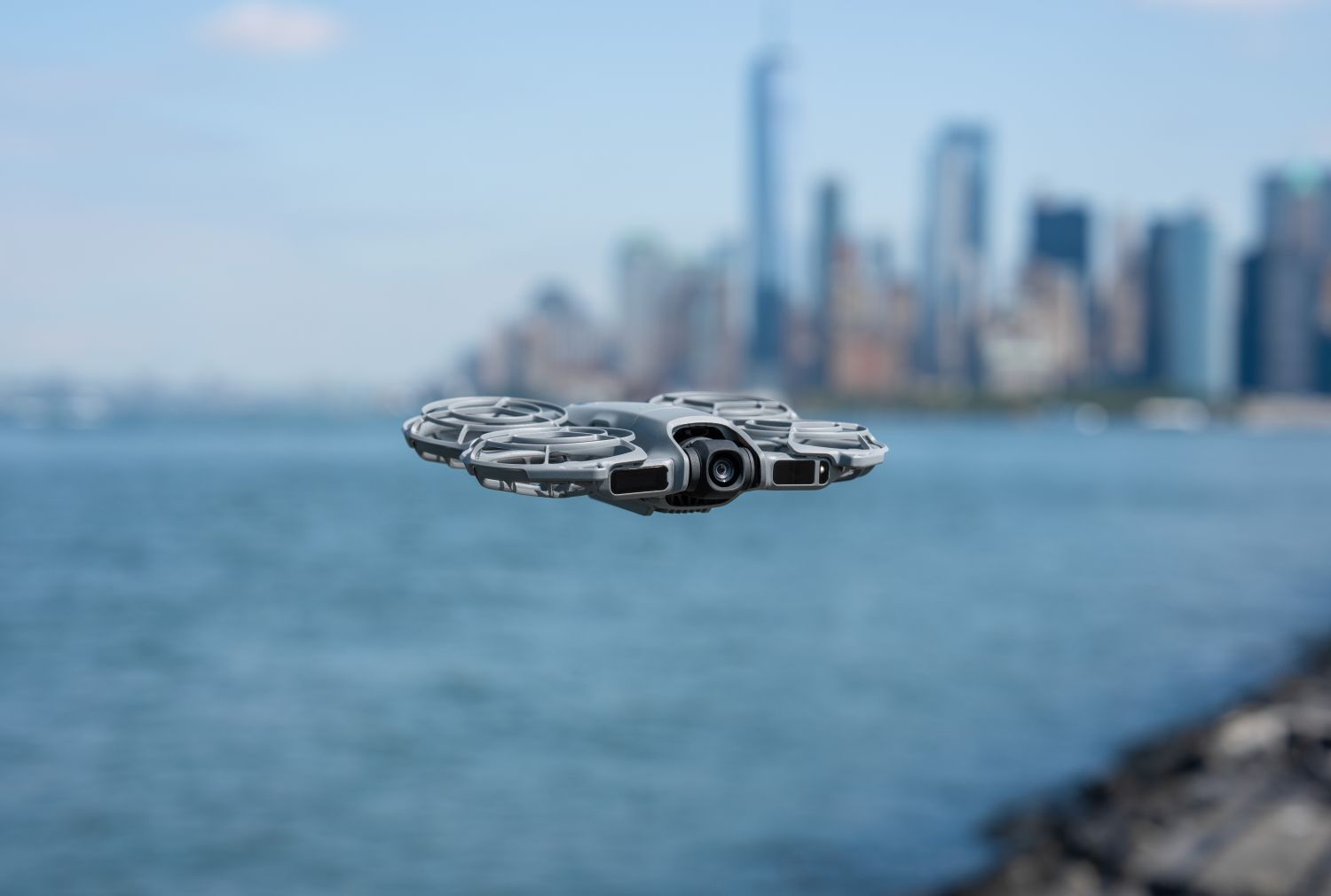 El DJI Neo 2 vuela sobre el agua con un skyline urbano desenfocado al fondo. La imagen transmite ligereza, estabilidad y estética cinematográfica.