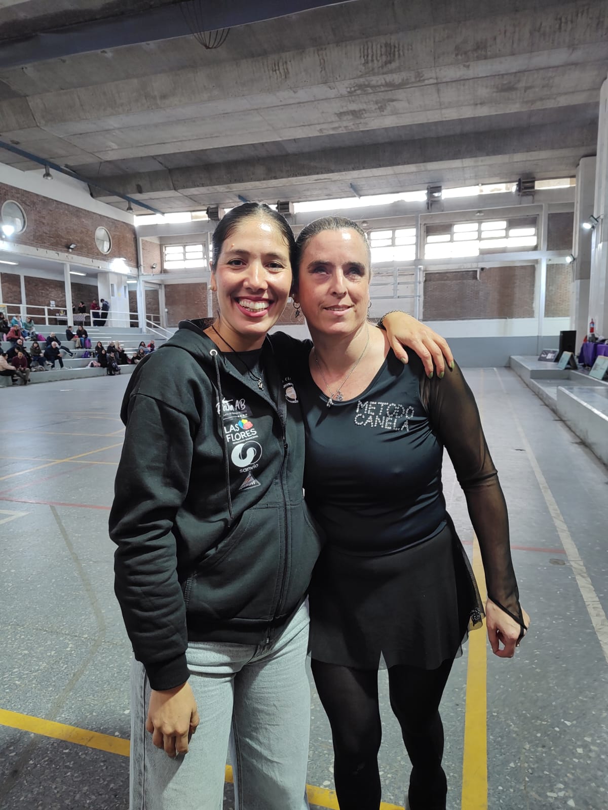 Ailen y Sol, posan juntas en el interior de una pista de patinaje, con las gradas y parte del recinto al fondo. Ambas visten prendas negras relacionadas con el Método Canela y aparecen sonrientes, abrazadas.
