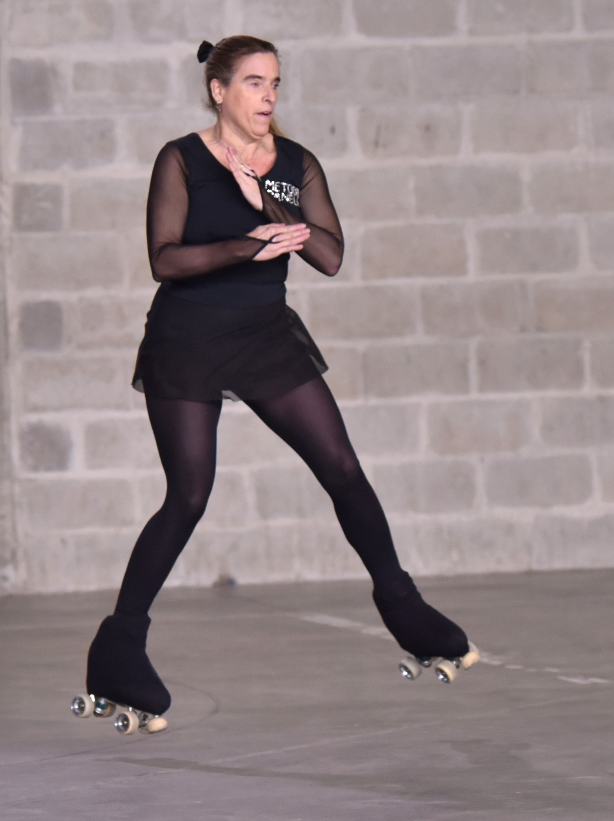 la patinadora Sol Campos realiza un salto sobre patines de cuatro ruedas, con ambos pies separados del suelo y las piernas extendidas. Viste completamente de negro y se encuentra en una pista cubierta, frente a una pared de bloques de hormigón.